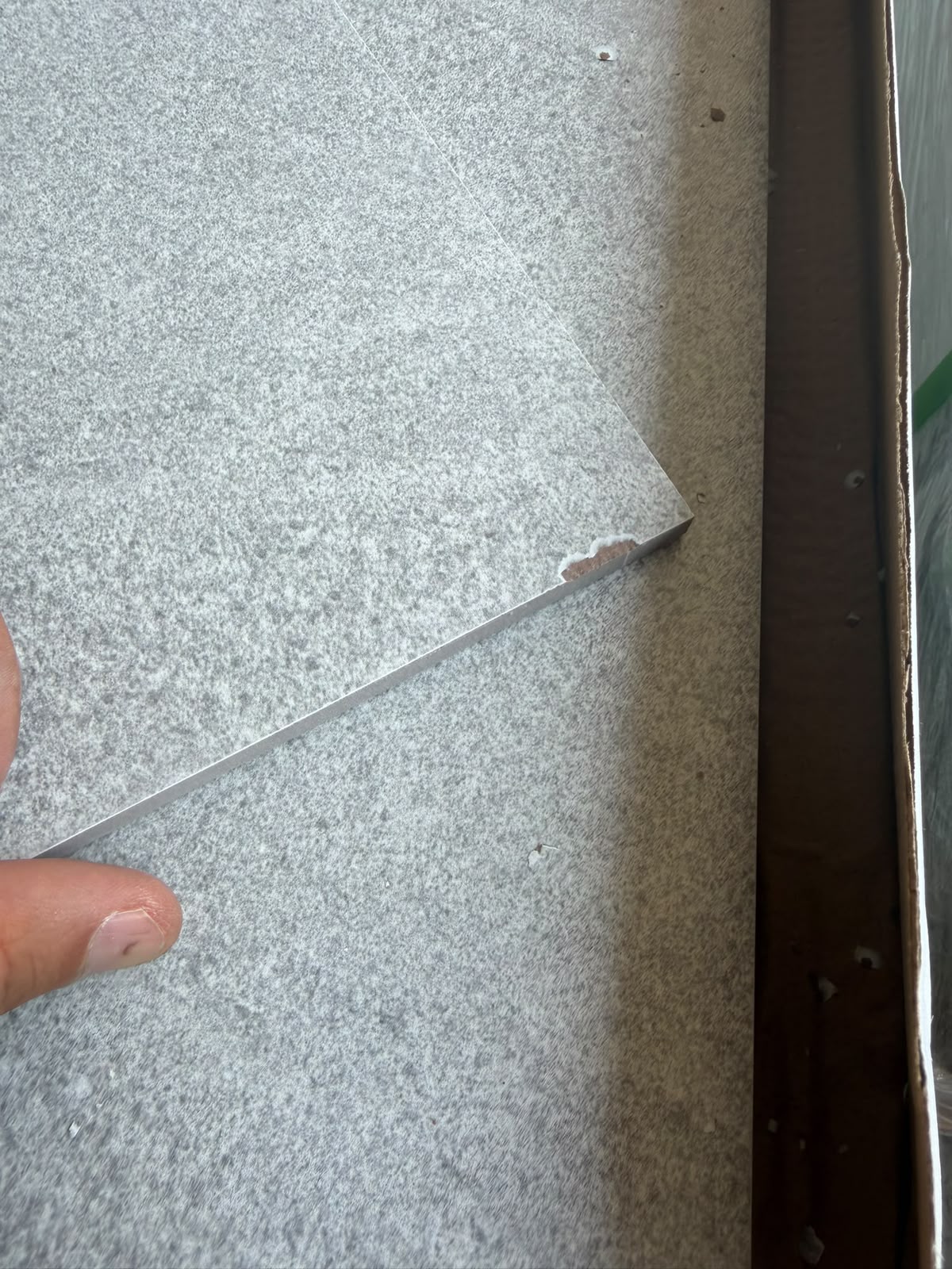 Angle d'un carreau de carrelage gris présentant un éclat, repéré pendant le contrôle qualité